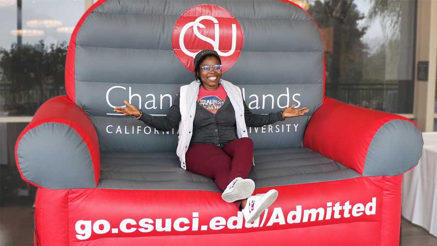 Female future CSUCI student siting on a chair that reads the address go.csuci.edu/Admitted
