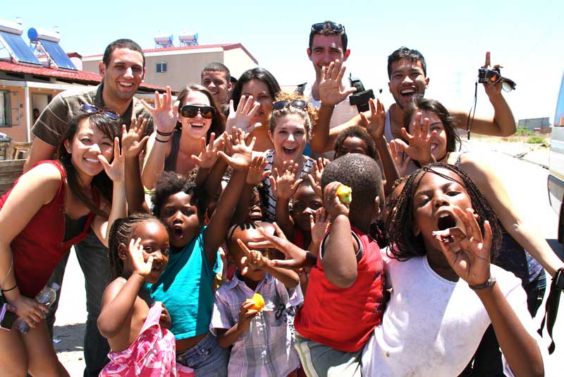 Group of students with children all smiling and waving at the camera