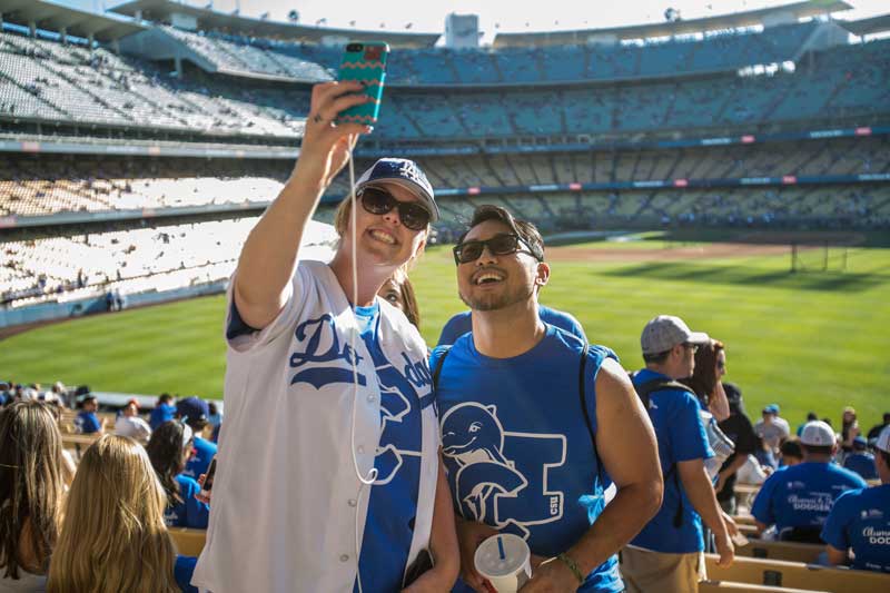 Two CI students wearing blue CI t-shirts taking a selfie at a baseball base game