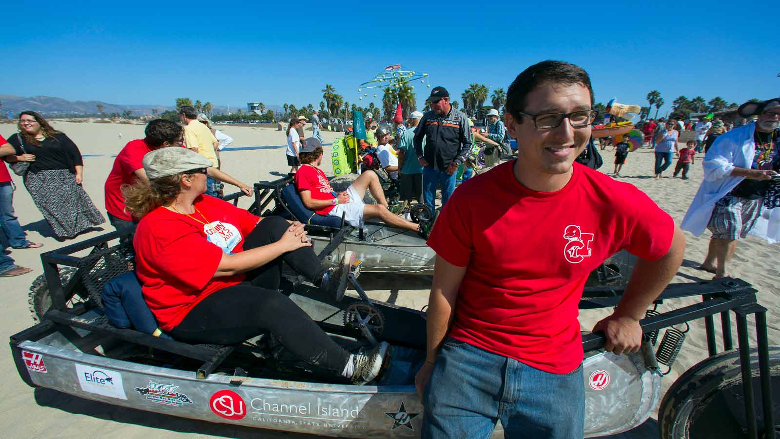 Student wearing a red tshirt in a go kart and another student leaning on the front of the go kart on the beach