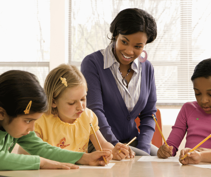 Teacher and Students smiling teacher sitting with students at a desk