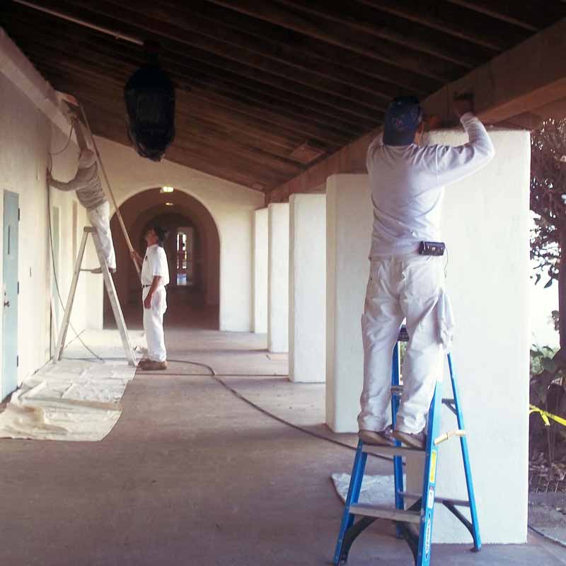 two men painting building on campus