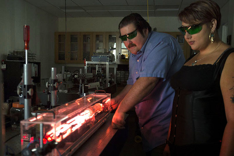 Man and woman wearing protective glasses to look at a glowing red light in a lab