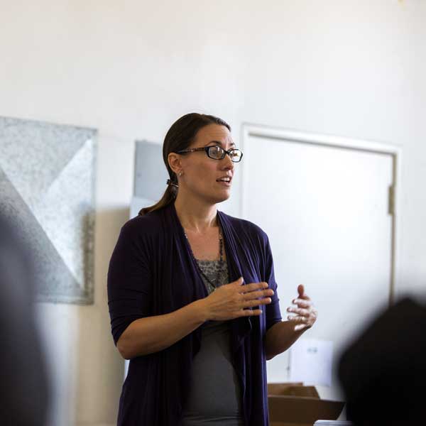 Woman wearing glasses giving a lecture wearing a purple cardigan