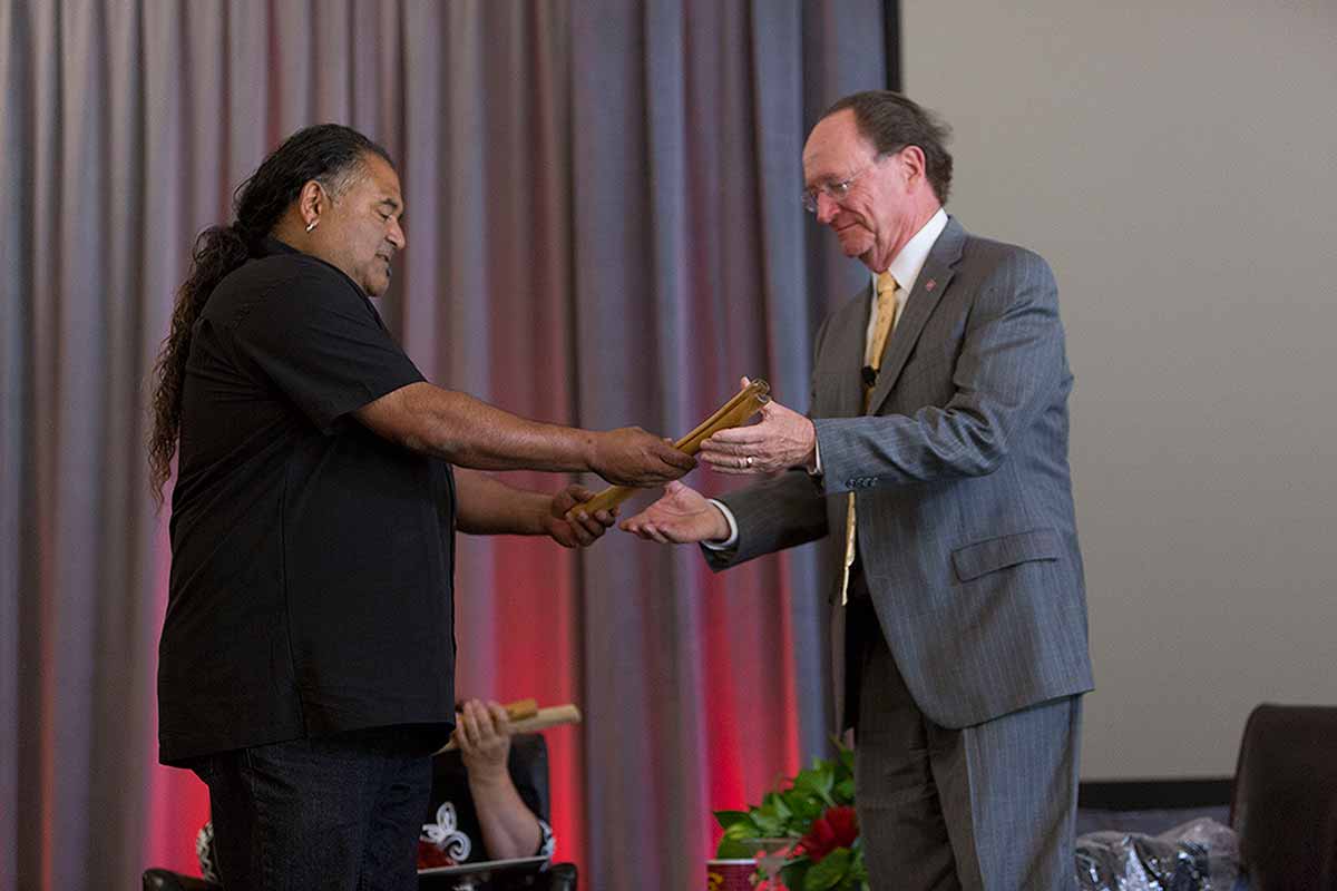 Raudel Bañuelos, a tribal member of The Barbareño/Ventureño Band of Mission Indians and CI’s Director of Facilities Support, presents to President Rush a handmade clapperstick, also known as a wansak’. 