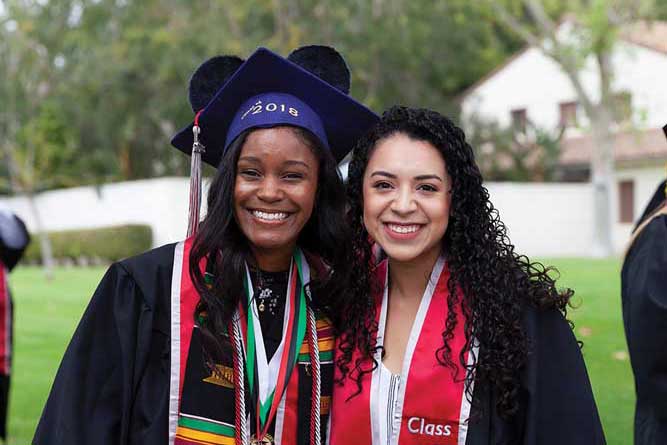 Two graduates smile and pose together at the 2018 commencement
