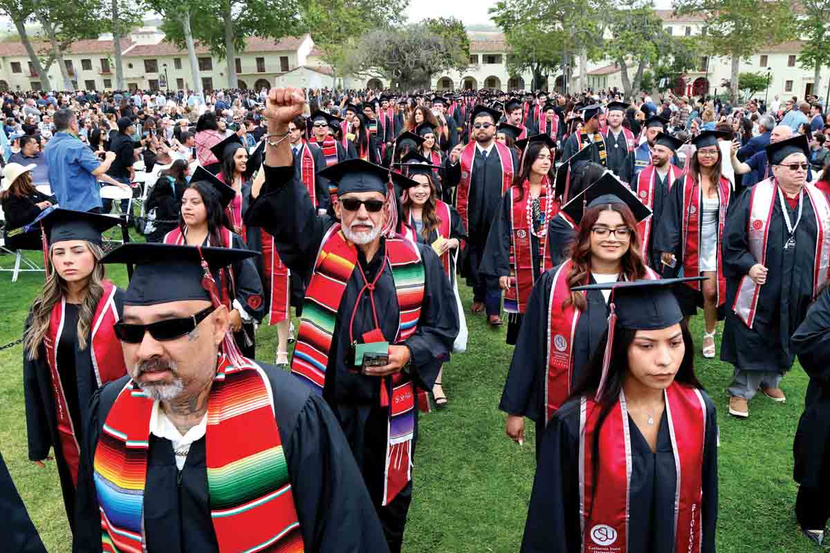 ose Rodriguez Sr., B.A. Art, gives a victory fist pump as he walks behind his son (front left) Jose Rodriguez, Jr., B.A. Sociology, as they process with other graduates as part of this year's Commencement ceremony. 