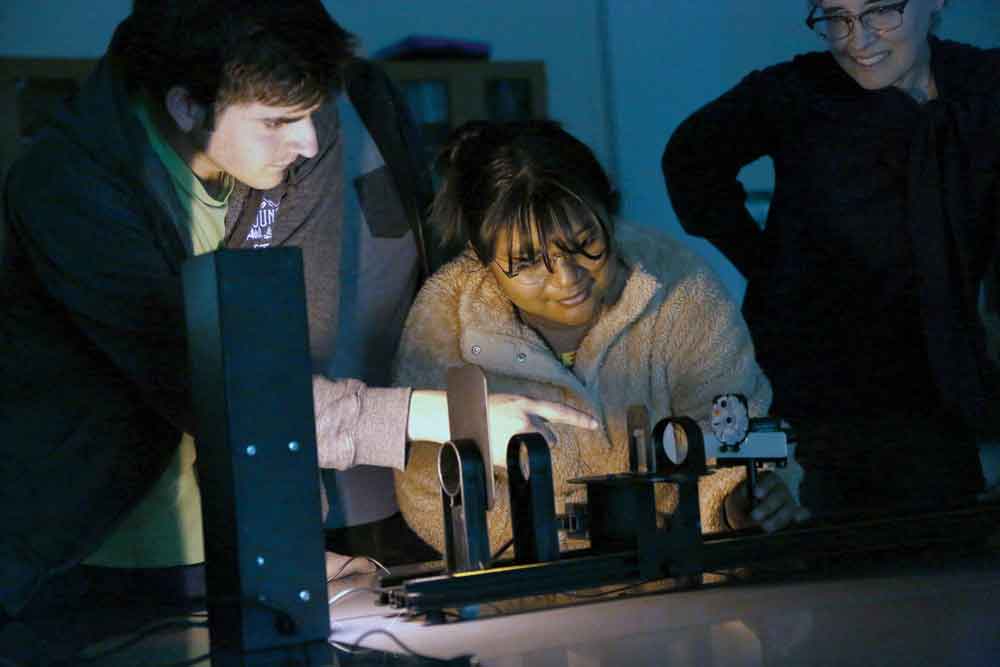 Physics students Seth Curtin and Jasmine Torres, along with lecturer Tabitha Swan-Wood explaining how an Atomic Spectra Defractometer works.