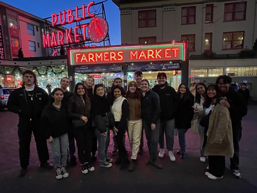 Students stand in front of the "Public Market" sign in Seattle