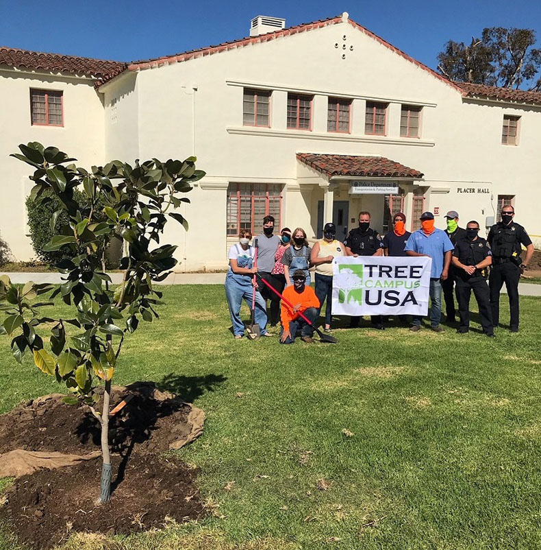 Police Department employees stand with Facilities members with Tree Campus USA banner and newly planted tree