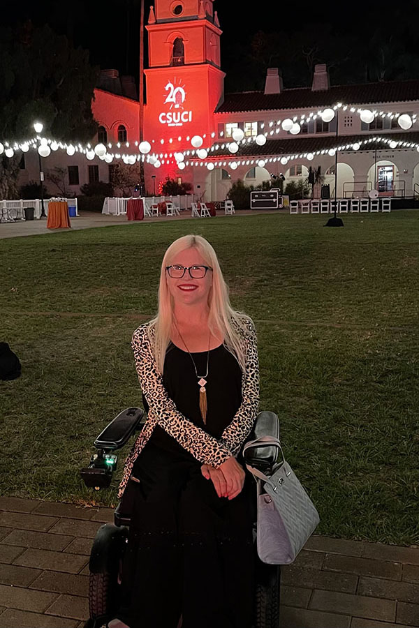 Dani Anderson poses in front of the Bell Tower lit up with the 20th Anniversary logo.