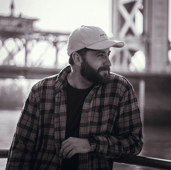 a portrait of Zach Valladon in front of a bridge