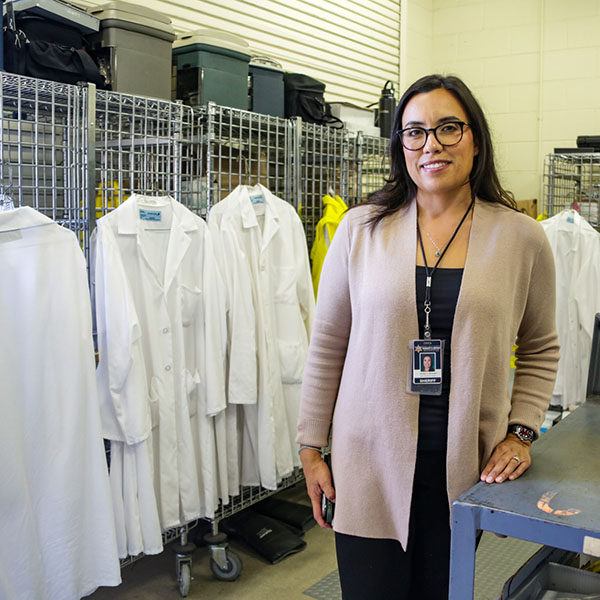 Dennise Hernadez stands next to a metal workshop table with lab coats behind her