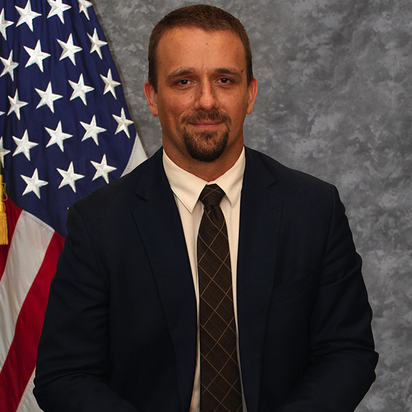 Photo is a portrait of Robert J. Stukes next to an American flag