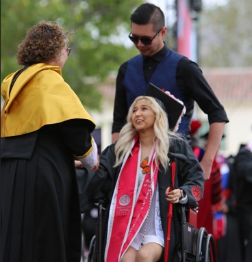 Graduating student using wheelchair receiving diploma on graduation stage