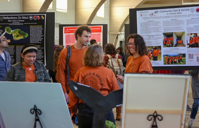 Students stand in a group at the CCE Celebration of Service in front of a student research poster.