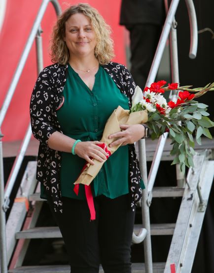 jessica stands smiling with a bouquet of red and white flowers