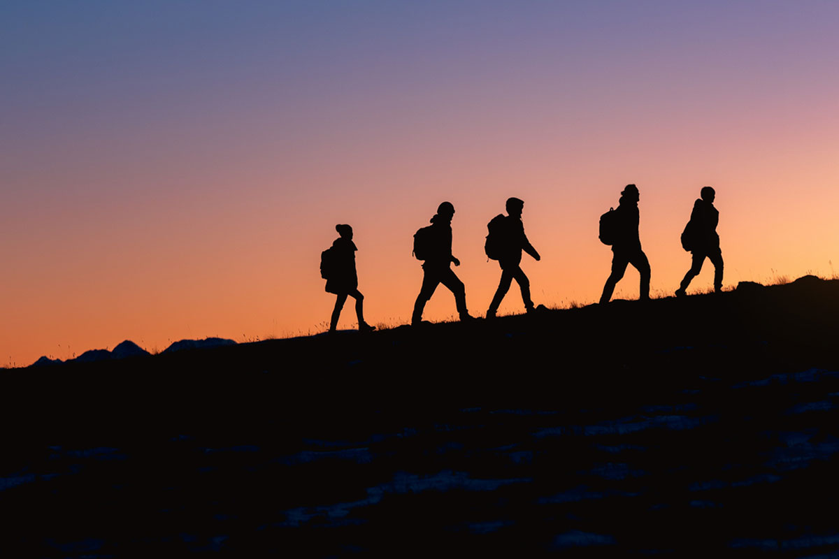 5 people hiking up an incline with a purple and orange sunset seen in the background.
