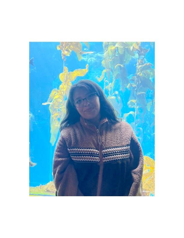 Jazlyn is wearing a black cowboys hat and has black rimmed glasses. she is staring straight at the camera. she has wavy brown hair.