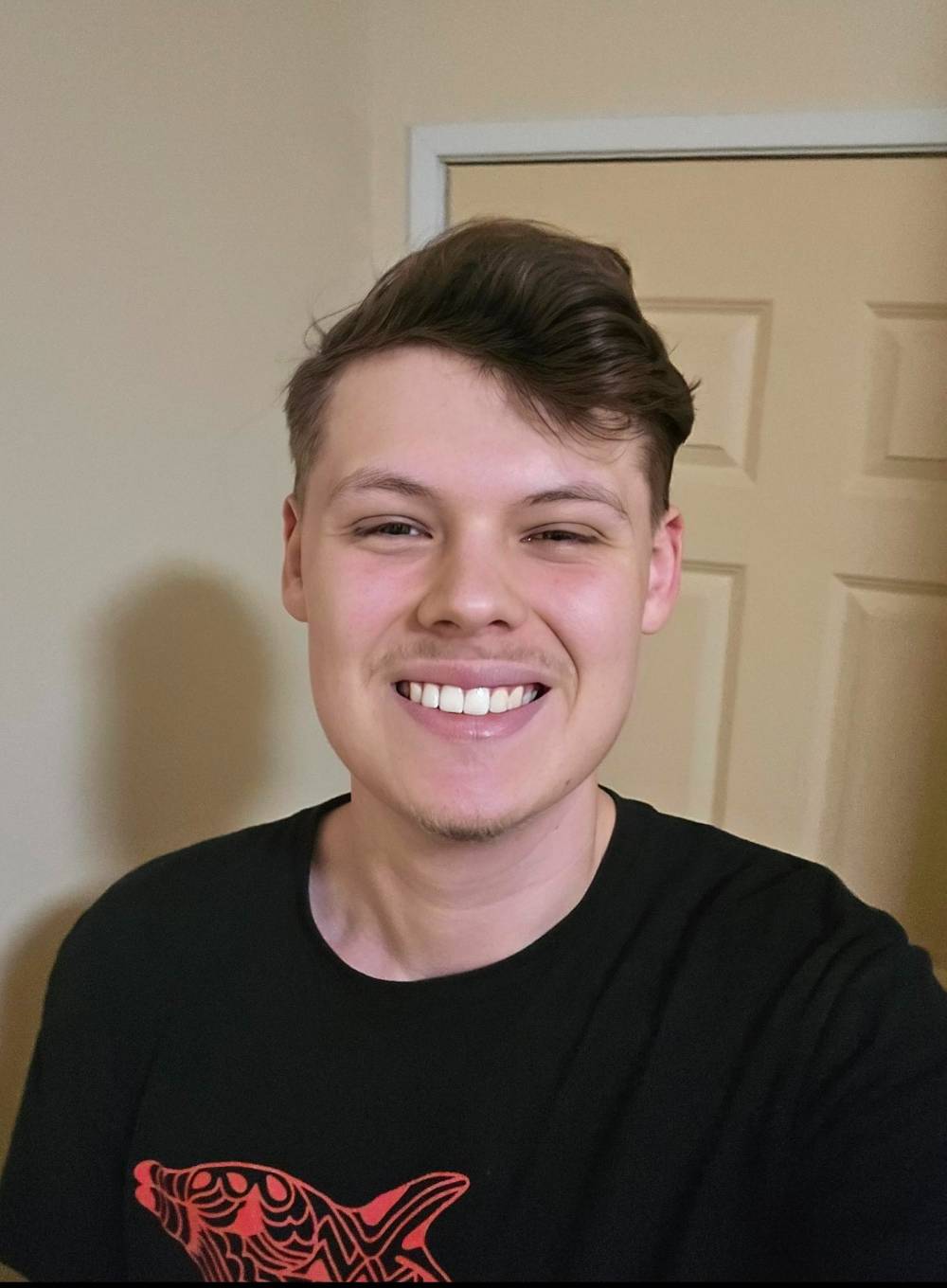 Ethan has short brown hair and is wearing a black shirt with a red fish on it