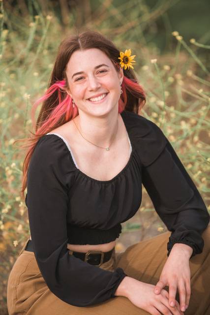 Kira has red hair and yellow flowers in it. She is wearing a long sleeved black shirt